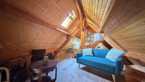 Ein gemütliches Dachzimmer mit Holzwänden, einem blauen Sofa, einem kleinen Tisch und einer Lampe.