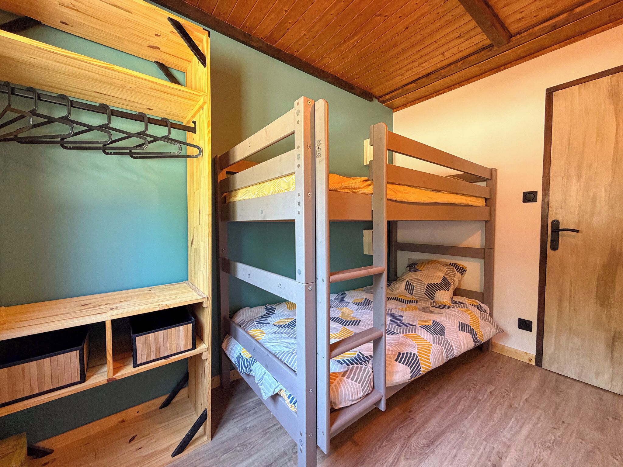 A bunk bed with a wooden frame and a lower shelf with storage boxes, a door, and a wall-mounted coat rack.