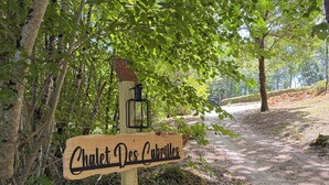 Ein hölzernes Wegweiser mit der Aufschrift 'Chalet Des Cabrilles', ein Laternenmast und ein Pfad durch ein bewaldetes Gebiet.