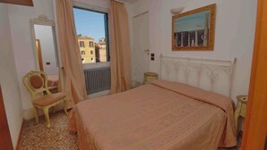 A bedroom with a bed, a chair, a radiator, a window with curtains, and a painting on the wall.