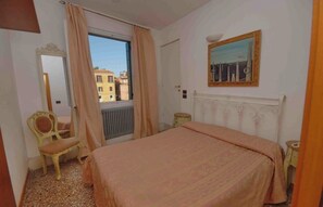 A bedroom with a bed, a chair, a radiator, a window with curtains, and a painting on the wall. - Vrbo Property (Venezia)