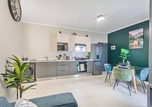 A modern kitchen with a dining area, a clock, and a green wall with a painting. - Zalari Luxe 93 on New, 1 Bed, Central & Premium Comfort (Johannesburg)
