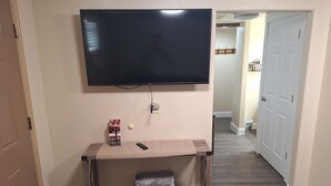 A room with a TV mounted on the wall, a small table with a remote, a cushion, and a wall socket. - Beautiful 1-bedroom cabin with AC in charming Glendale (Glendale)