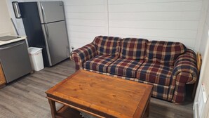 A compact living space with a kitchenette, a plaid sofa, and a wooden coffee table. - Beautiful 1-bedroom cabin with AC in charming Glendale (Glendale)