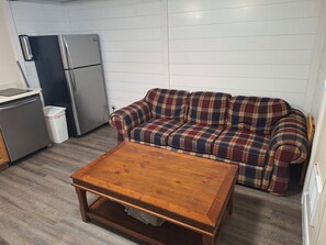 Ein kompakter Wohnbereich mit Küchenzeile, einem karierten Sofa und einem Holztisch.