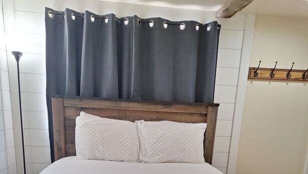 A bed with a wooden headboard, white bedding, and a dark curtain. - Beautiful 1-bedroom cabin with AC in charming Glendale (Glendale)