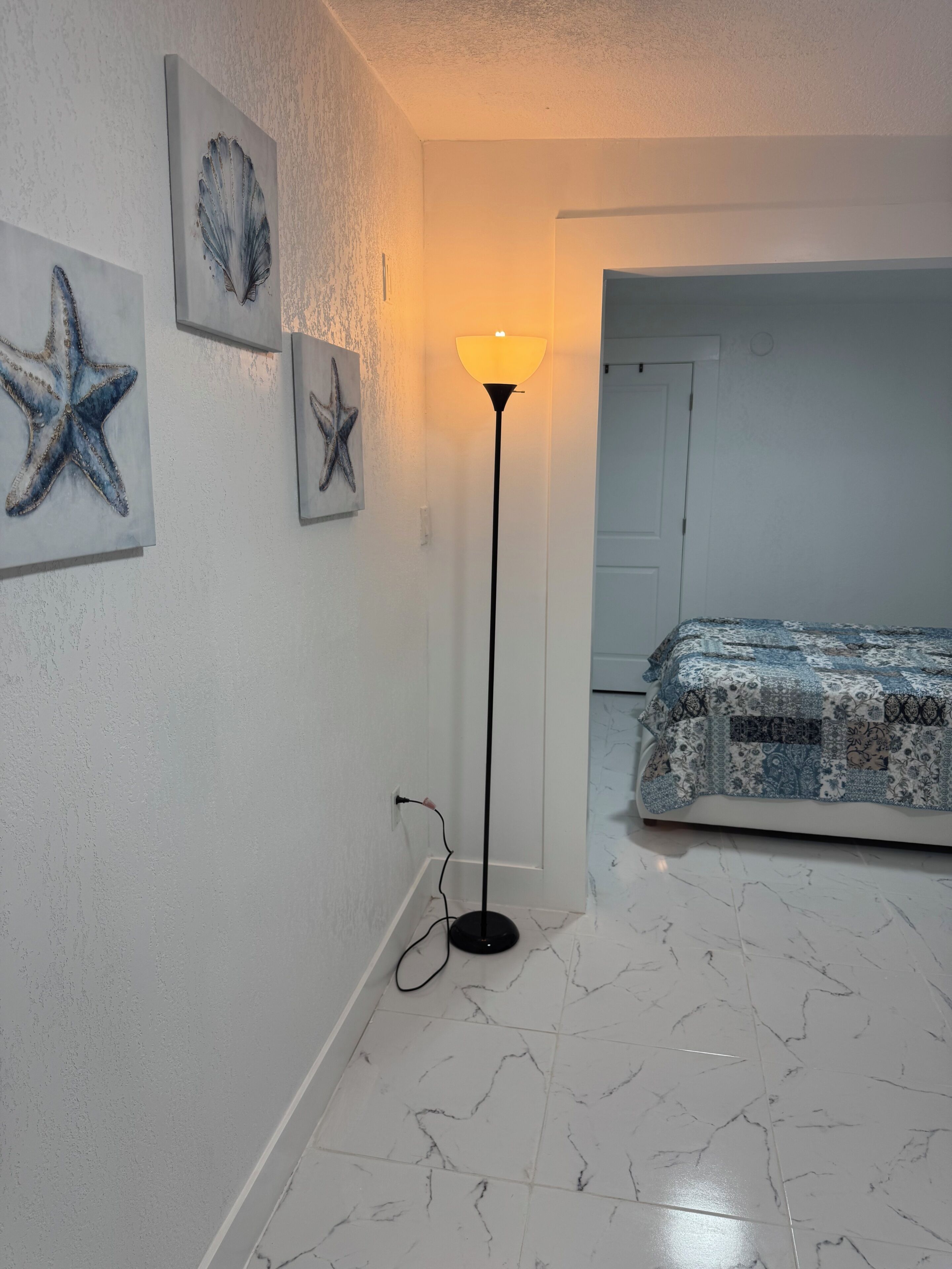 A room with a bed, a standing lamp, and starfish artwork on the wall.