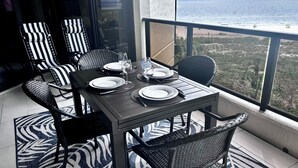 Un coin repas avec une table dressée pour quatre personnes, des chaises et une vue sur l’océan.