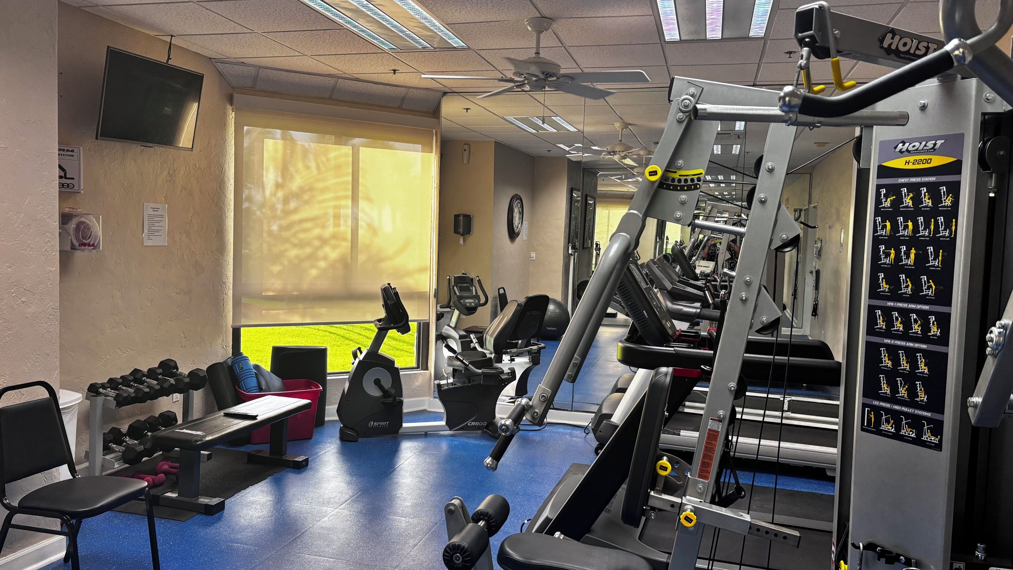 A gym with exercise equipment, a treadmill, dumbbells, and a wall-mounted instructional chart.