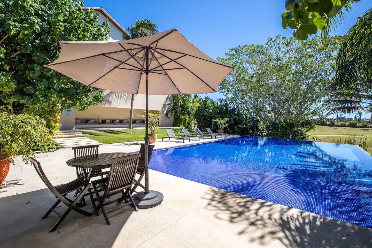 A swimming pool with a patio area, including a table and chairs, and an umbrella.