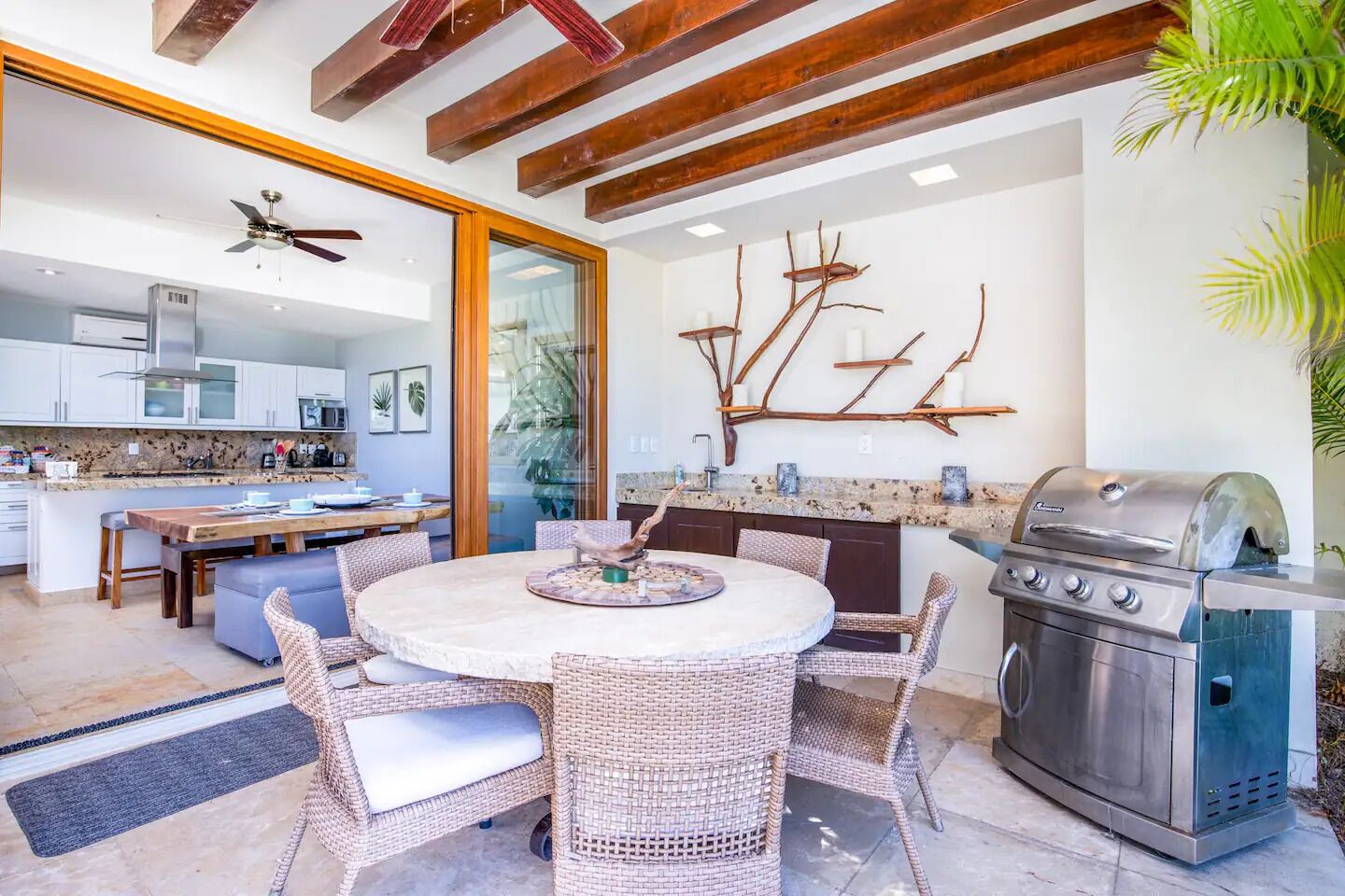 A modern kitchen with a built-in grill, a dining area with wicker furniture, and a large window.