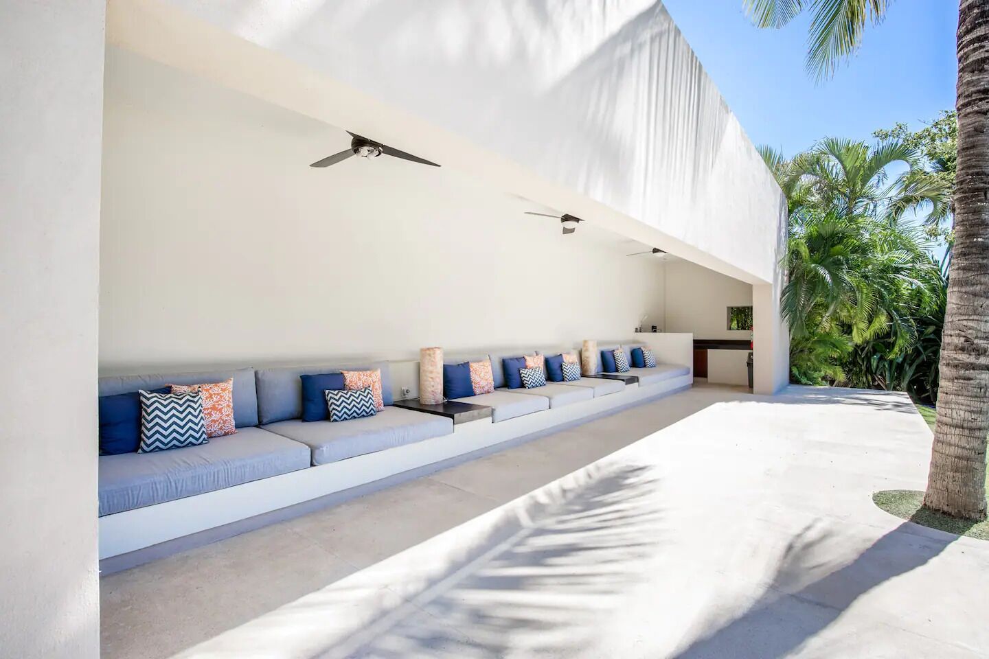 A modern outdoor seating area with a sofa, pillows, and ceiling fans.
