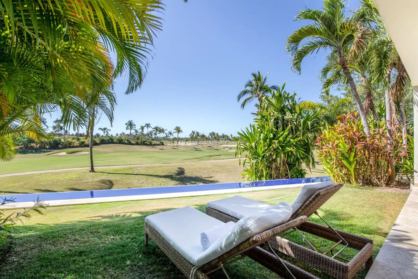 A lounge chair on a balcony with a view of a golf course and palm trees.