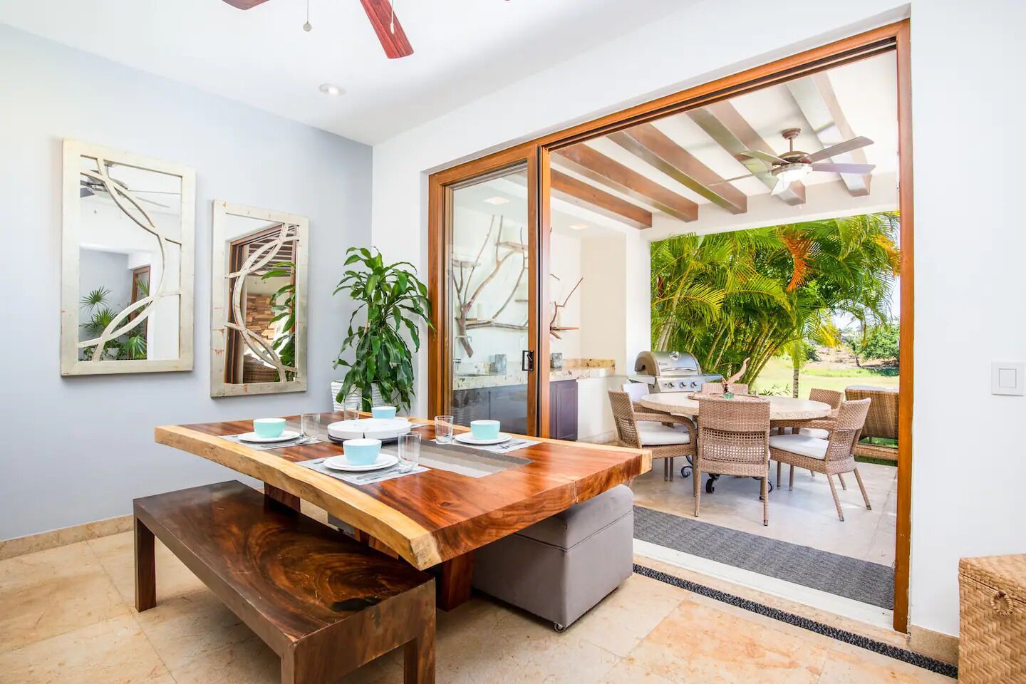 Un área de comedor con una mesa de madera, sillas y vistas al exterior a través de un ventanal.