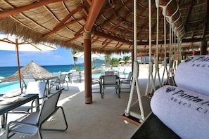 Eine Strandbar mit Reetdach, Liegestühlen und einem Pool.