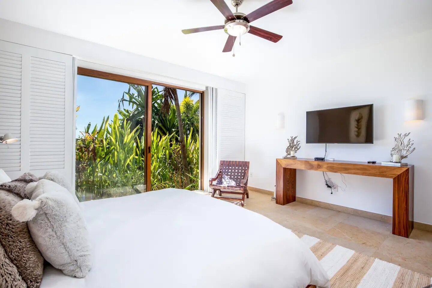 A bedroom with a bed, a desk, a chair, a TV, and a ceiling fan.