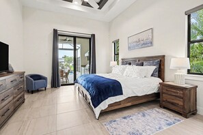 Une chambre à coucher comprenant un lit, une table de chevet, un téléviseur, une chaise et une porte-fenêtre coulissante donnant sur un espace extérieur.