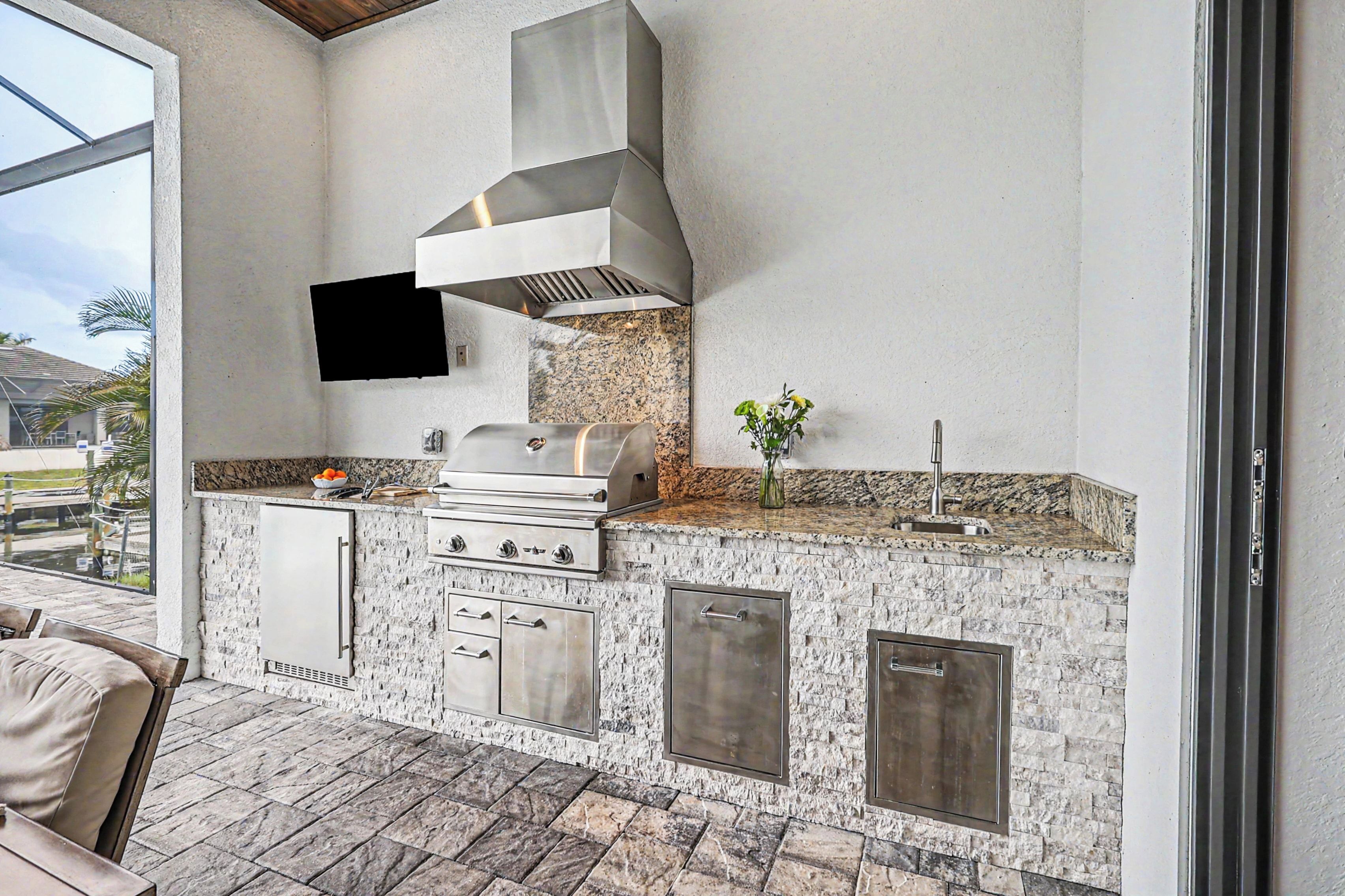 An outdoor kitchen with a grill, built-in cabinets, and a stone backsplash.