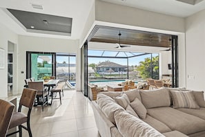 Ein modernes Wohnzimmer mit einer großen Couch, Essbereich und Blick auf einen Swimmingpool.