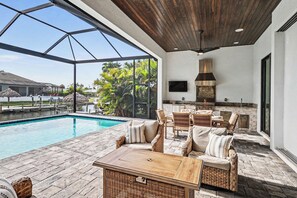 Une terrasse extérieure avec une piscine, des meubles en osier, un barbecue et un téléviseur fixé au mur.