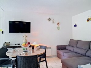 Ein Wohnzimmer mit einer Couch, einem Esstisch mit Stühlen, einem an der Wand befestigten Fernseher und einem Wandheizkörper.