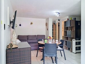 Ein Wohnzimmer mit einer Couch, einem Esstisch mit Stühlen, einem Fernseher und einem Bücherregal.
