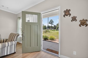 A room with a door leading to a view of a grassy area, a striped armchair, and three turtle wall decorations. - Napping Turtle a serene 4-bedroom +bonus room. with AC in charming Springfield (Springfield)