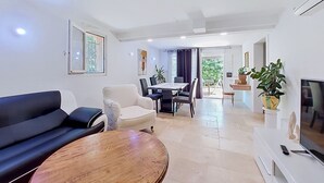 A modern living room with a sofa, dining table, chairs, and a TV. - Bas de villa Anémones by Interhome (Bormes-les-Mimosas)