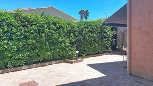 A stone patio with a hedge, a metal manhole cover, and a white chair. - Bas de villa Anémones by Interhome (Bormes-les-Mimosas)