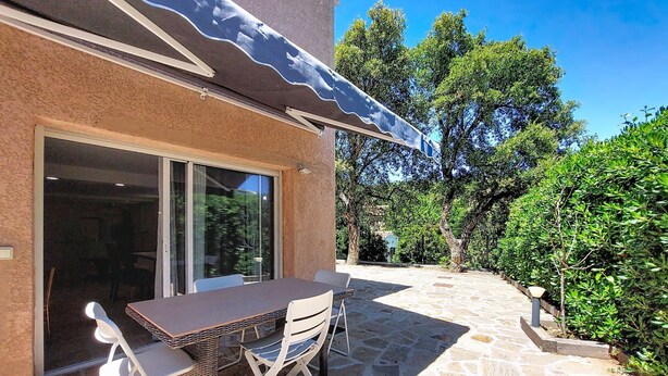 A patio with a table and chairs, a glass door, and a stone floor. - Bas de villa Anémones by Interhome (Bormes-les-Mimosas)