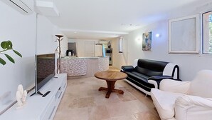 A modern living room with a sofa, a TV, a dining table, and a kitchen in the background. - Bas de villa Anémones by Interhome (Bormes-les-Mimosas)