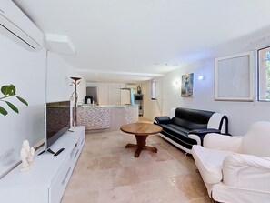 Ein modernes Wohnzimmer mit einer Couch, einem Fernseher, einem Esstisch und einer Küche im Hintergrund.