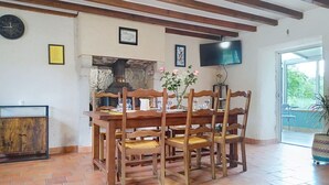 A dining area with a wooden table, chairs, a brick floor, a TV on the wall, and a window with a view. - L'ancienne Ferme by Interhome (Lestre)