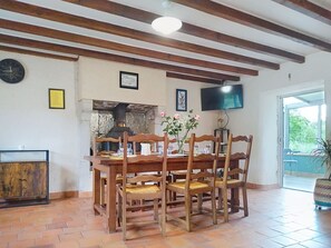 Ein Essbereich mit Holztisch, Stühlen, Steinboden, einem Fernseher an der Wand und einem Fenster mit Aussicht.