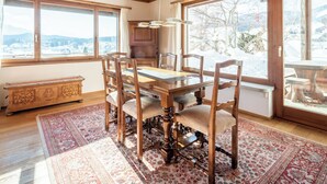 A dining room with a wooden table and chairs, a rug, and large windows with a snowy view.