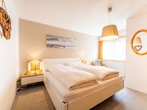 A modern hotel room with a large bed, bedside lamps, a wall-mounted picture, a window with curtains, and a circular wall decoration. - Crap Uaul by Interhome (Flims)