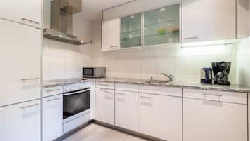 A modern kitchen with white cabinetry, a microwave, an oven, a coffee maker, and a glass-fronted cabinet.