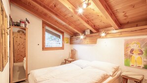 Une chambre avec un plafond en bois, un lit, une fenêtre, une chaise et un tableau accroché au mur.