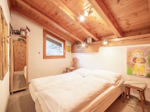 Een slaapkamer met een houten plafond, een bed, een raam, een stoel en een schilderij aan de muur.