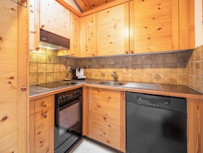 Een keuken met houten kastjes, een fornuis, oven, vaatwasser en een betegelde achterwand.