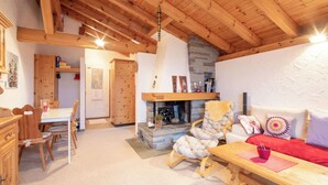 Un intérieur chaleureux avec un plafond en bois, une cheminée en pierre, un canapé, une table à manger et des meubles en bois.