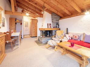 Een gezellig interieur met een houten plafond, een stenen openhaard, een bank, een eettafel en houten meubels.