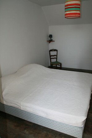 Een slaapkamer met een bed, een stoel, een plank met een lamp, en een gestreepte hanglamp.