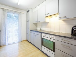 Eine moderne Küche mit weißen Schränken, einem Einbauofen, einer Spüle und einem Fenster mit durchsichtigen Vorhängen.