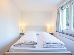 Ein Doppelbett mit weißer Bettwäsche, zwei Nachttische mit Lampen und ein Fenster mit Vorhängen.