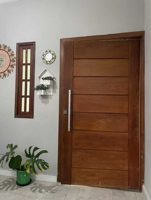 A wooden door with a handle, a potted plant, a wall-mounted mirror, and a decorative sunburst mirror. - Casa da Lu (Salvador)