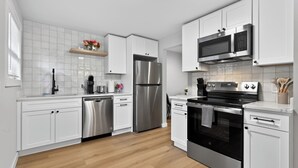A modern kitchen with white cabinetry, stainless steel appliances, and a wooden floor. - King Bed-Stadium District Getaway (Tacoma)