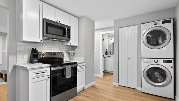 A modern kitchen with white cabinets, a microwave, an oven, and a stacked washer and dryer. - King Bed-Stadium District Getaway (Tacoma)