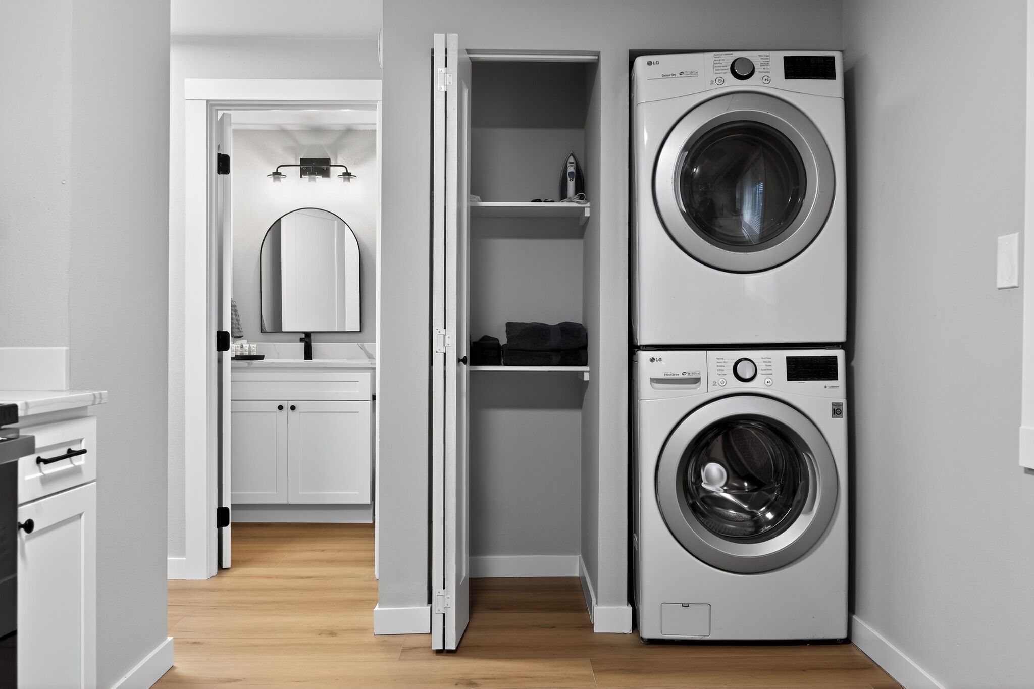 Une buanderie équipée d’un lave-linge et d’un sèche-linge superposés, d’un miroir et d’une petite étagère sur laquelle sont posés divers objets.