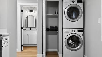 Une buanderie équipée d’un lave-linge et d’un sèche-linge superposés, d’un miroir et d’une petite étagère sur laquelle sont posés divers objets.